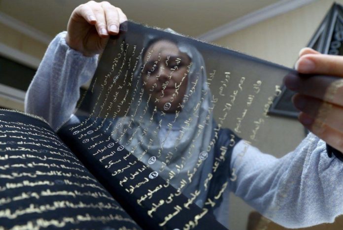 Une femme brode à la main une copie entière du Noble Coran sur de la soie pure